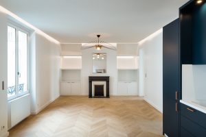 Grande chambre blanche avec meubles bleus et parquet en chevron